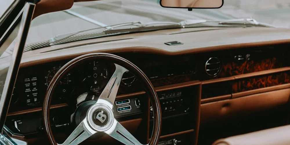 Close-up of a vintage car interior with brown leather dashboard, steering wheel, and wood trim