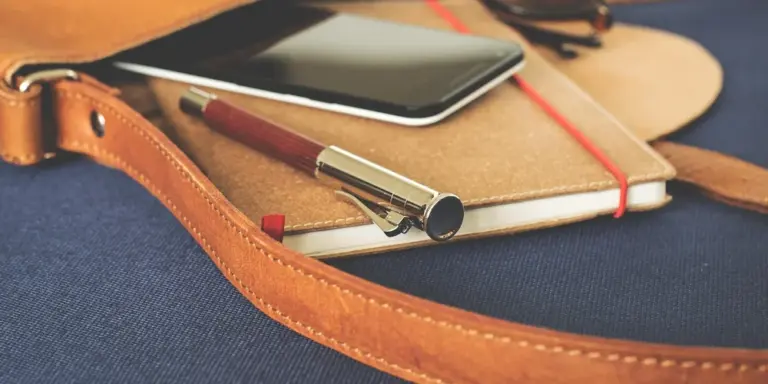 Close-up of a tan leather strap resting on a notebook with a smartphone on a dark blue fabric surface.