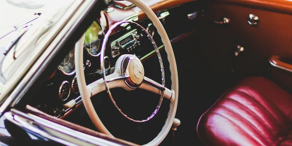 Close-up of a vintage car interior featuring a cream steering wheel and rich brown leather seats.