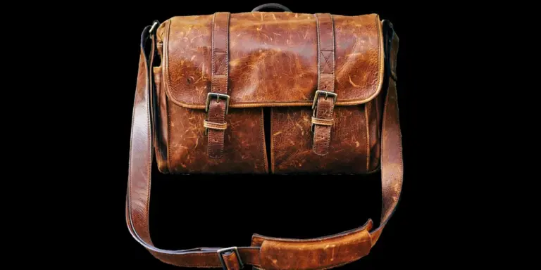 A vintage brown leather satchel with a shoulder strap against a black background.