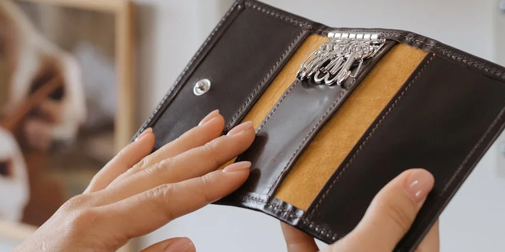 Hands hold an open leather wallet showing its interior compartments, illustrating care after reshaping or repair.