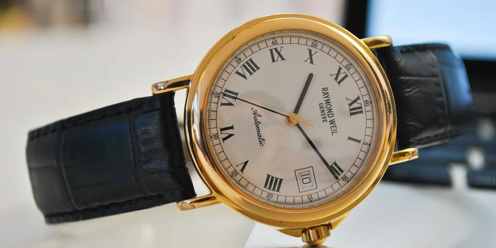 Close-up of a gold watch with a black leather strap, highlighting leather items that require conditioning.