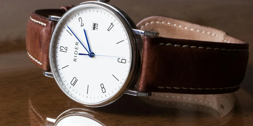 Brown leather watch strap with white stitching on a wooden surface