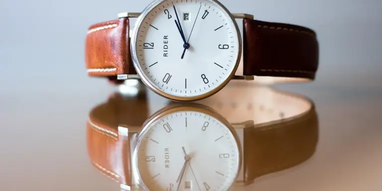 Close-up of a wristwatch with a brown leather strap reflected on a glossy surface.