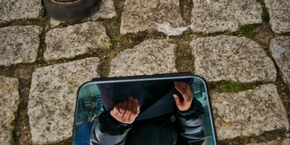 Close-up of a cobblestone ground with a dark boot at the edge, suggesting rainy conditions and the need to care for suede footwear.