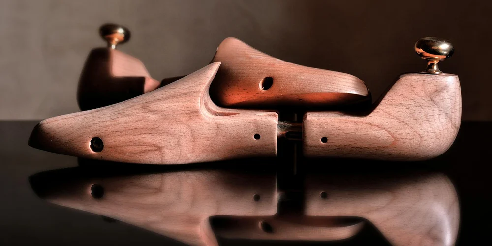 Two wooden shoe lasts resting on a dark, reflective surface.